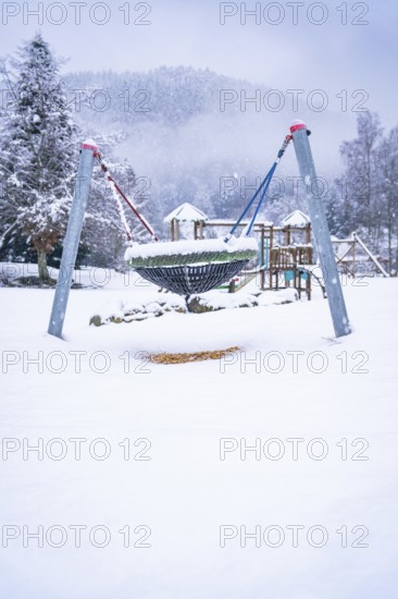 A snow-covered playground equipment on a snowy square, surrounded by fog-covered trees, Enzklösterle, Calw district, Black Forest, Germany, Europe
