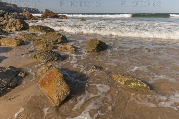 A rocky beach with a large rock in the foreground and a boat in the distance. The beach is quiet and peaceful, with the water. Camaret sur mer, Crozon, Finistere, Brittany, France, Europe