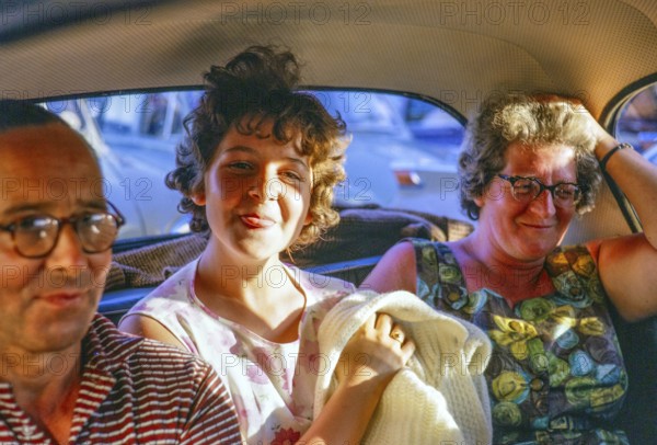 Junges Mädchen, das seine Zunge auf dem Rücksitz eines Familienautos herausstreckt, 1962
