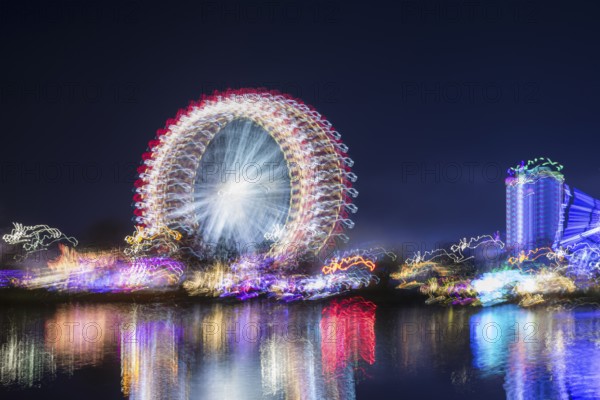 Atmospherically illuminated Ferris wheel and buildings are reflected blurred in the water, Blurred, Cannstadter Volksfest, Stuttgart, Baden-Württemberg