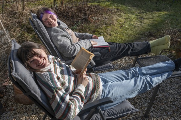 Two young woman in a deckchair reading in the garden, Bavaria, Germany, Europe
