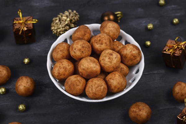 Traditional German Christmas sweets called Marzipankartoffeln. Round ball shaped almond paste pieces covered in cinnamon and cocoa powder in white bowl on dark background