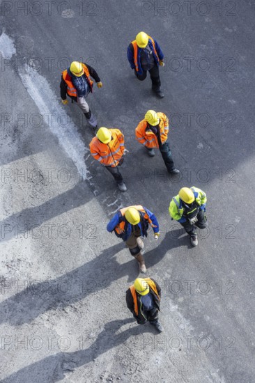 Several construction workers wearing hard hats walk over tarmac. They cast long shadows. Stuttgart, Baden-Württemberg, Germany, Europe
