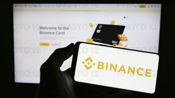 Stuttgart, Germany, 03-31-2023: Person holding mobile phone with logo of crypto exchange company Binance Holdings Ltd. on screen in front of web page. Focus on phone display, Europe