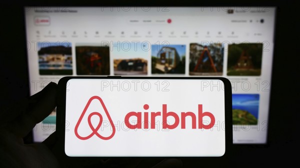 Stuttgart, Germany, 11-30-2022: Person holding smartphone with logo of US homestay marketplace company Airbnb Inc. on screen in front of website. Focus on phone display, Europe