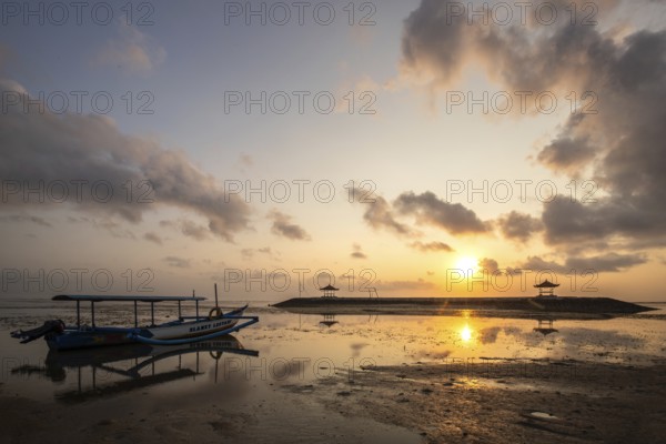 Morning landscape taken on the sandy beach. View over the sea to the horizon with small temples in the water and a jukung, a traditional fishing boat, on the beach. Sunrise in Sanur, Bali, Indonesia, Asia