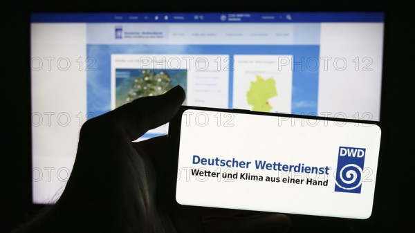 Stuttgart, Germany, 06-06-2024: Person holding mobile phone with logo of German meteorological service Deutscher Wetterdienst (DWD) in front of web page. Focus on phone display, Europe