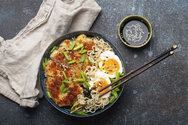 Asian noodles ramen soup with deep fried panko chicken fillet and boiled eggs in ceramic bowl with chop sticks and soy sauce on stone rustic background top view, food photography, food photography