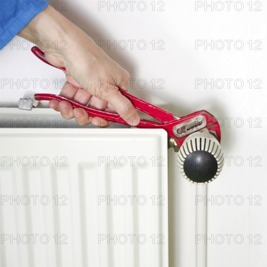Plumber fixing a radiator with red pliers