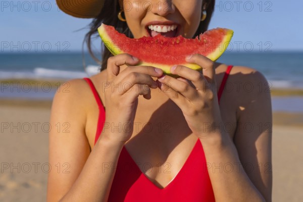 Portrait of a woman eating a watermelon by the beach. Cutout of mouth smiling with red bikini