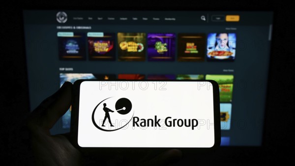 Stuttgart, Germany, 09-15-2022: Person holding smartphone with logo of British gambling company The Rank Group plc on screen in front of website. Focus on phone display, Europe