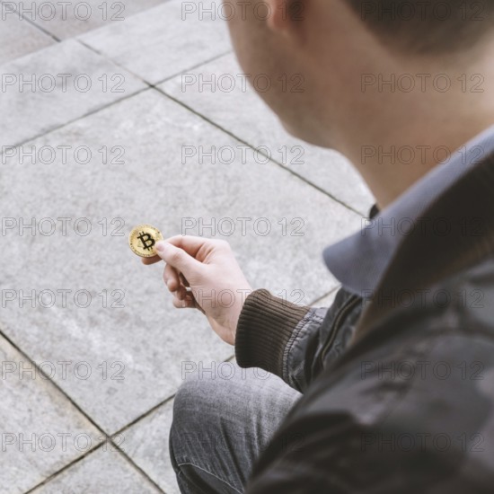 unrecognizable young man holding bitcoin coin in his hand, cryptocurrency hype concept