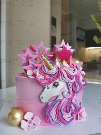 A whimsical unicorn birthday cake with pink and gold decorations, featuring pastel flowers and star accents