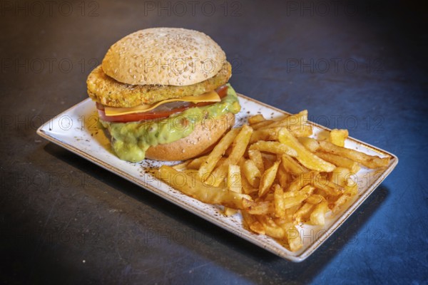 Vegan burger with guacamole and fries on a white plate on a black background