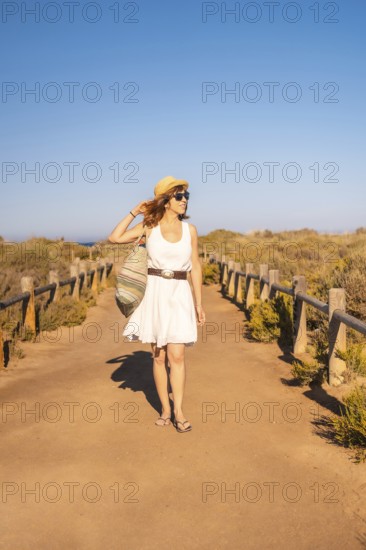 Vertical photo of a woman walking with a beach bag along a marked trail in Cabo de Gata, Spain, Europe