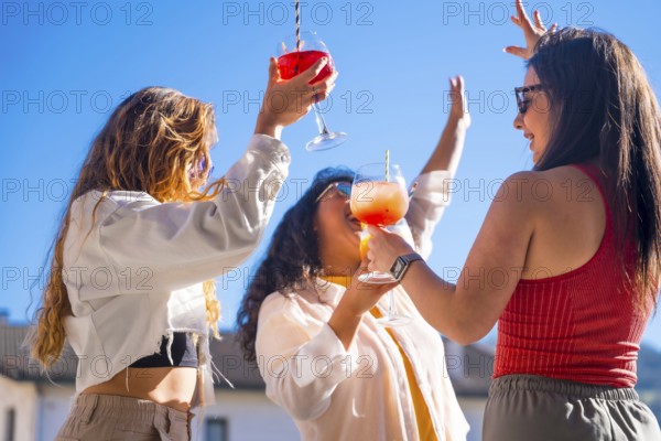 Three women dancing and drinking alcohol at the roof party in summer