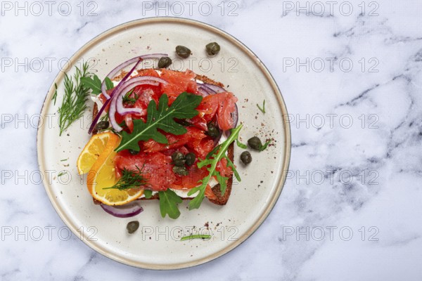 Sandwich with freshly smoked salmon, on black bread, with cottage cheese, with herbs and red onions, capers and pieces of citrus fruits, on a marble countertop, breakfast, no people