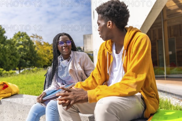 Side view of two male and female african students chatting relaxed in the campus sitting on a bench