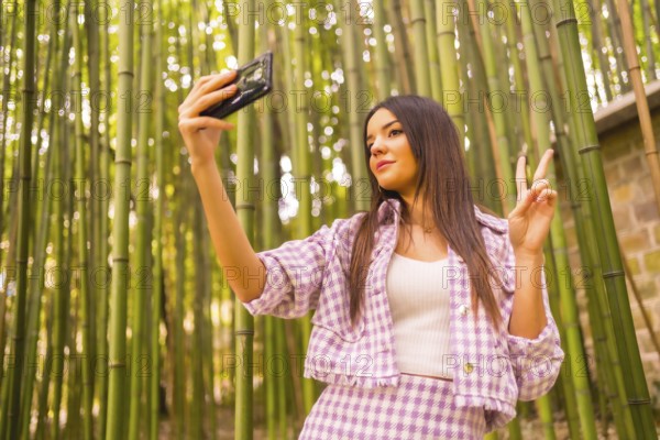 Young caucasian girl with a pink skirt in a bamboo forest. Enjoying summer holidays in a tropical climate, a girl lifestyle doing a selfie in the forest