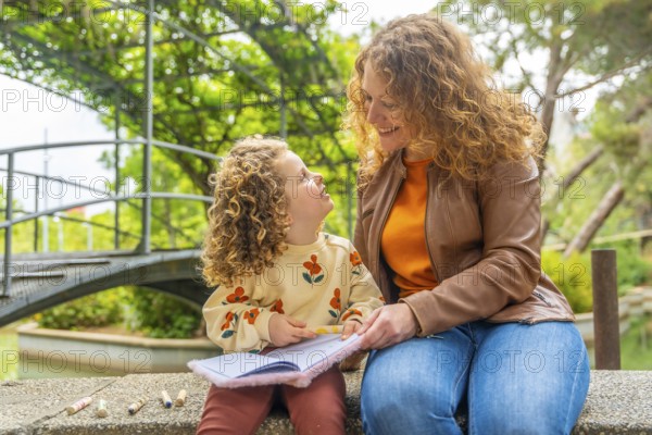 Cute blonde girl reading a book with her mother in the park