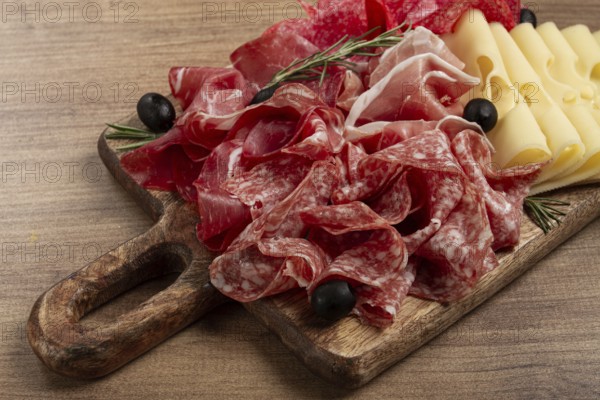 Assorted meat, appetizer, prosciutto, salami and ham, with maasdam cheese and olives, on a wooden board, breakfast, top view, close-up, no people