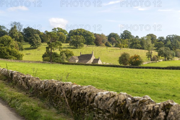 Cotswolds landscape of fields, trees, farmhouse building, near Yanworth, Gloucestershire, England, UK dry stone wall foreground