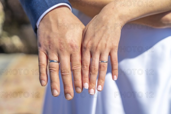 A couple is holding hands and wearing wedding rings. The man's ring is on the left hand and the woman's ring is on the right hand