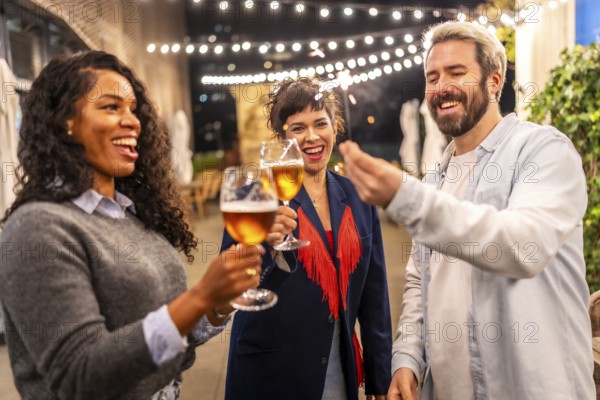 Multi-ethnic friends toasting with beer and holding sparklers while enjoying a night party