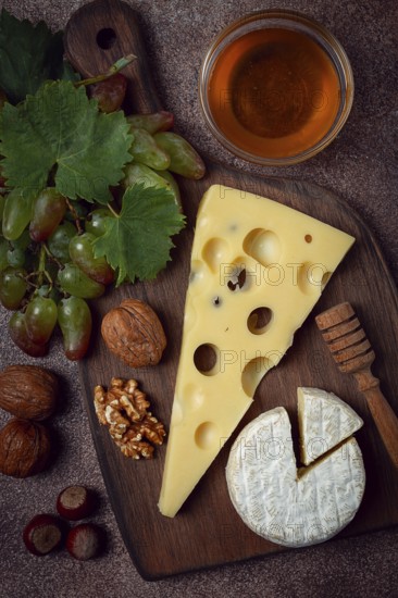 Cheese with big holes, emmental, maasdam, brie cheese, on a cutting board, with grapes and honey, nuts, appetizer to wine, top view
