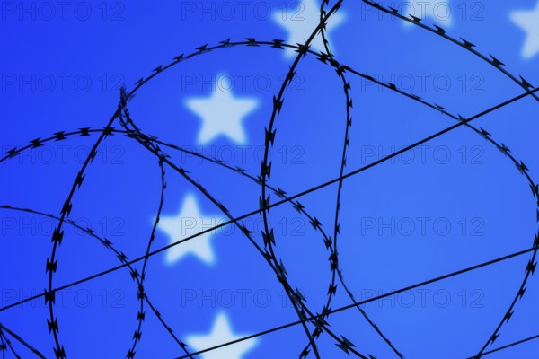 Symbolic image, migration, defence against refugees wanting to enter the EU, barbed wire overarches the stars of the EU flag against a blue sky, border, border fence