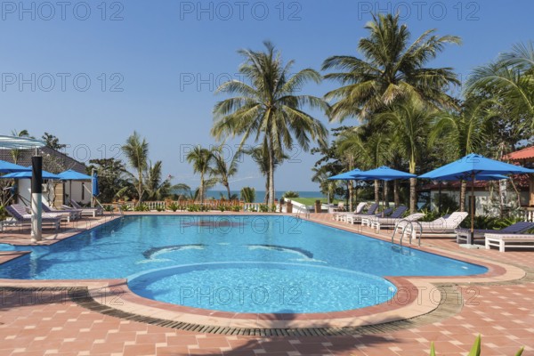 Swimming pool in tropical resort with palm trees and sea on horizon