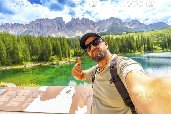 Tourist enjoying the breathtaking view of lake carezza and the dolomites making selfie and thumbs up