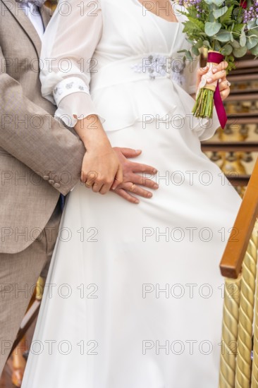 A bride and groom are standing on a staircase, the bride holding a bouquet of flowers. Scene is romantic and happy, as the couple is celebrating their wedding day