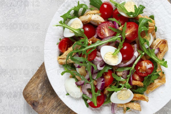A warm salad with fried chicken fillet, arugula and cherry tomatoes, and boiled quail eggs, on a white plate, no people