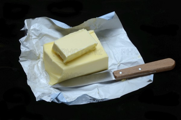 A piece of butter with packaging and kitchen knife