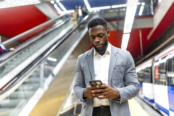 Young businessman waiting for a subway train in a station, using his smartphone to check messages and stay connected while commuting