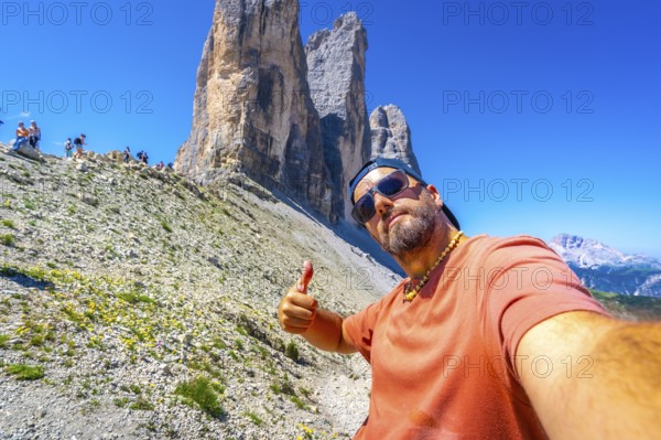 Tourist taking a selfie and making thumbs up gesture while hiking in the tre cime di lavaredo, dolomites, italy, during summer