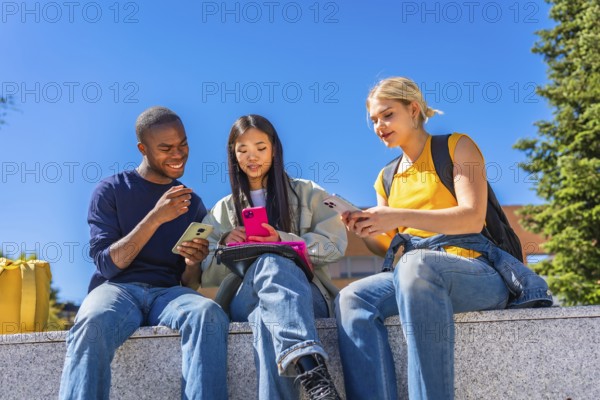 Low angle view photo of a multiracial group of students using smartphones sitting outside the campus