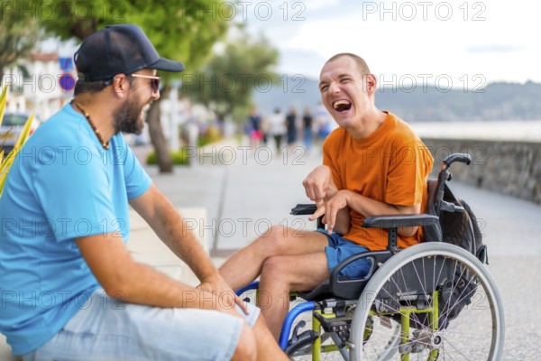 A disabled person in a wheelchair with a friend on summer vacation having fun laughing a lot by the sea