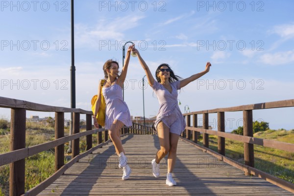 Female friends on summer vacation at the beach walking on a wooden path walking and jumping with excitement