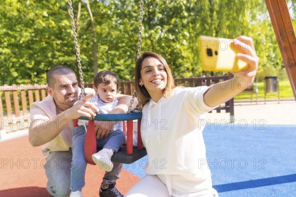 Happy family taking selfie in a playground with a baby boy in a sunny day