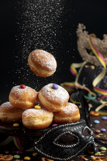 Doughnuts are sprinkled with icing sugar, surrounded by a mask and colourful decorations, carnival