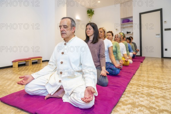 Yoga teacher leading a group of women meditating in line in lotus position and eyes closed