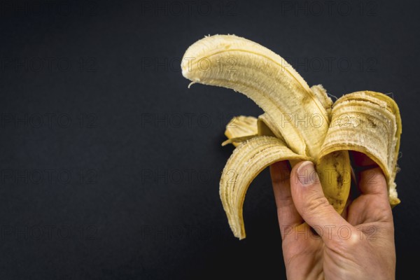 A peeled banana in a woman's hand on a black background