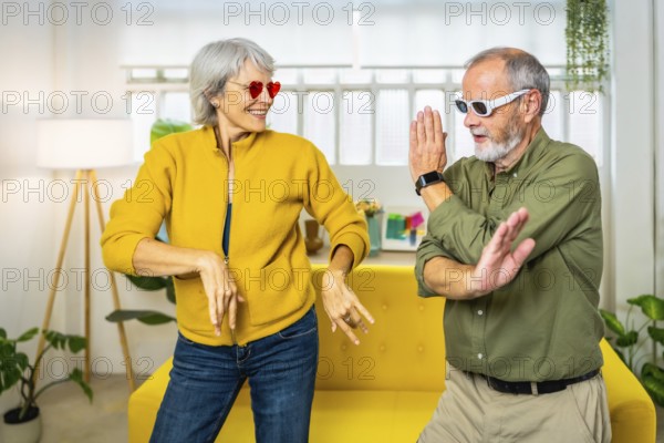 Frontal three quarter length photo of a caucasian married senior couple dancing wearing modern sunglasses at home