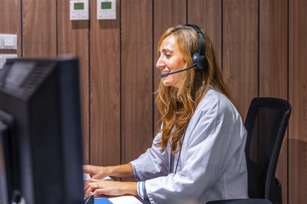 Hospital nurse receptionist talking to patient at registration counter using headset and computer