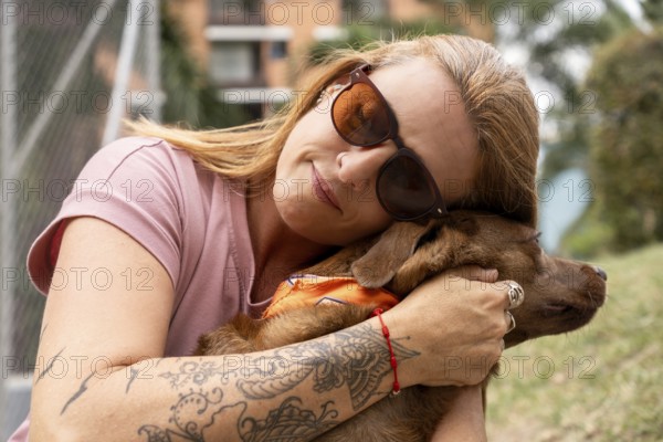Close-up of a woman with closed eyes and sunglasses hugging her dog affectionately