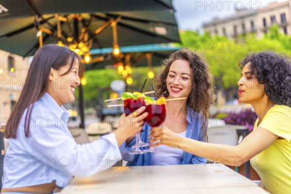 Three multi-ethnic female friends toasting with cocktails enjoying summer in the city
