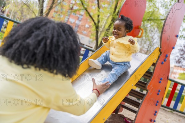 Happy african child playing with her mother in the slide in a public playground