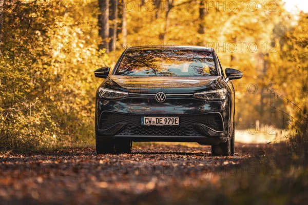Car on forest road in autumn with colourful leaves and yellow light, electric car VW ID5, Gechingen, Black Forest, Germany, Europe